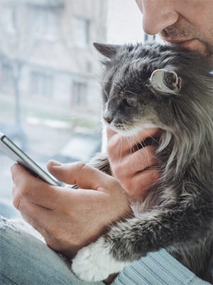 a man holding a cat in his lap while looking at his mobile phone